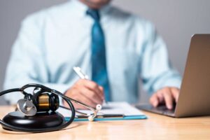 A person reviews car insurance documents at a kitchen table with a cup of coffee and laptop.